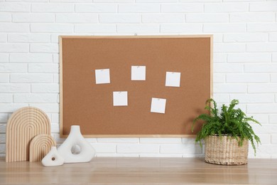 Photo of Cork board with blank paper notes and decorative elements on wooden table near white brick wall