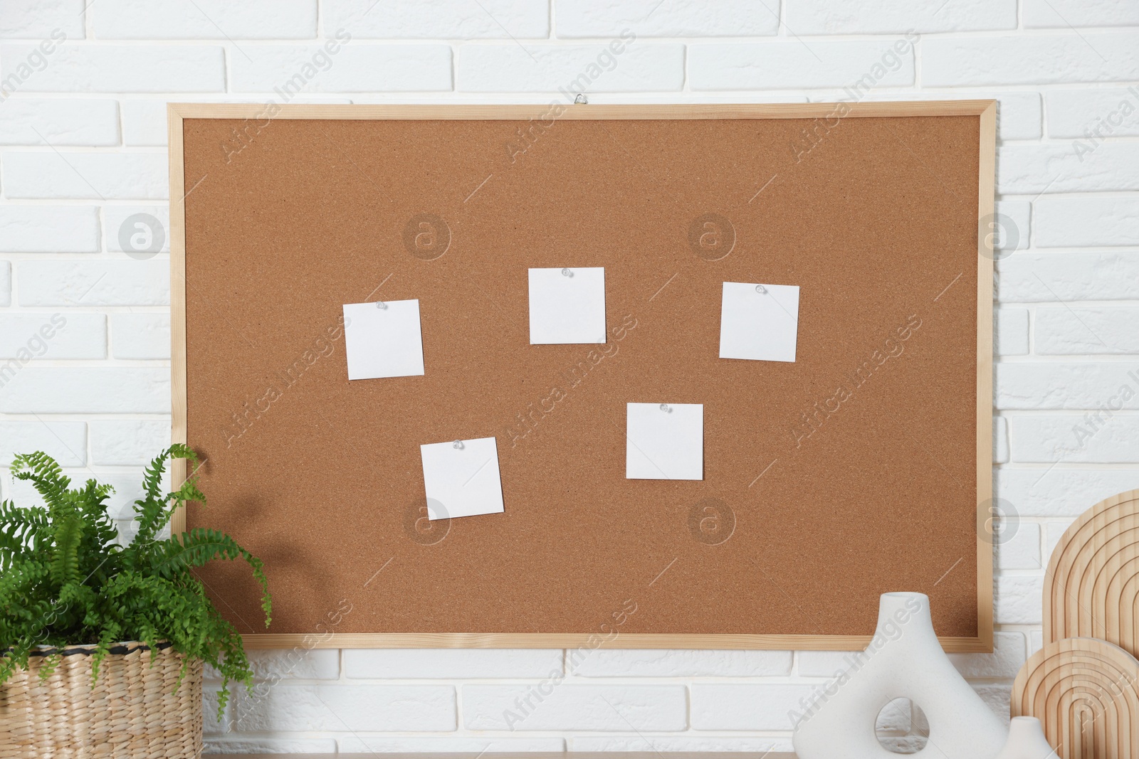 Photo of Cork board with blank paper notes and decorative elements near white brick wall