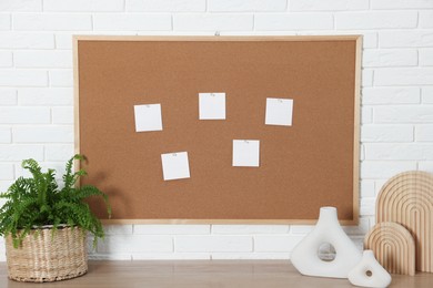 Photo of Cork board with blank paper notes and decorative elements on wooden table near white brick wall