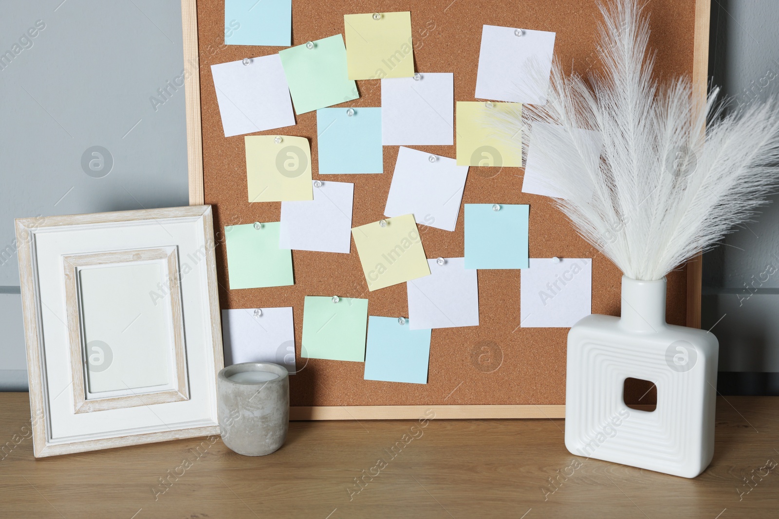 Photo of Cork board with blank paper notes and decorative elements on wooden table near gray wall