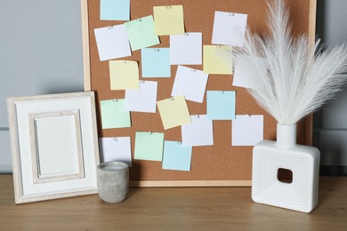 Cork board with blank paper notes and decorative elements on wooden table near gray wall