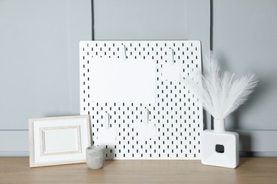 Photo of Peg board with blank paper notes and decorative elements on wooden table near gray wall