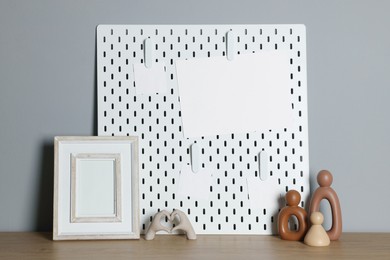 Peg board with blank paper notes and decorative elements on wooden table near gray wall