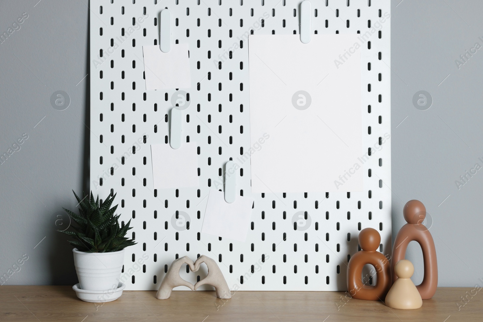 Photo of Peg board with blank paper notes and decorative elements on wooden table near gray wall