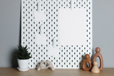 Photo of Peg board with blank paper notes and decorative elements on wooden table near gray wall