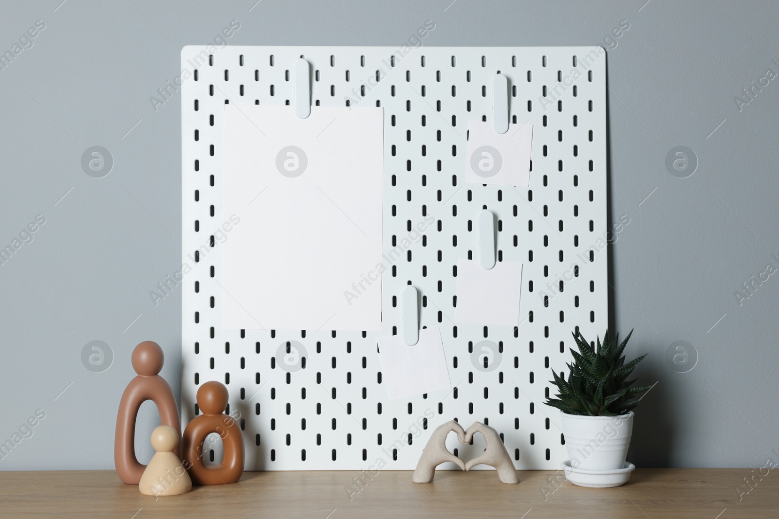 Photo of Peg board with blank paper notes and decorative elements on wooden table near gray wall