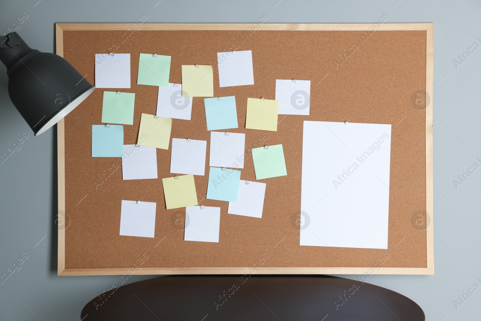 Photo of Cork board with blank paper notes, lamp and black table gray wall