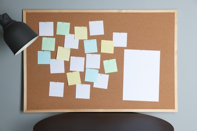 Photo of Cork board with blank paper notes, lamp and black table gray wall