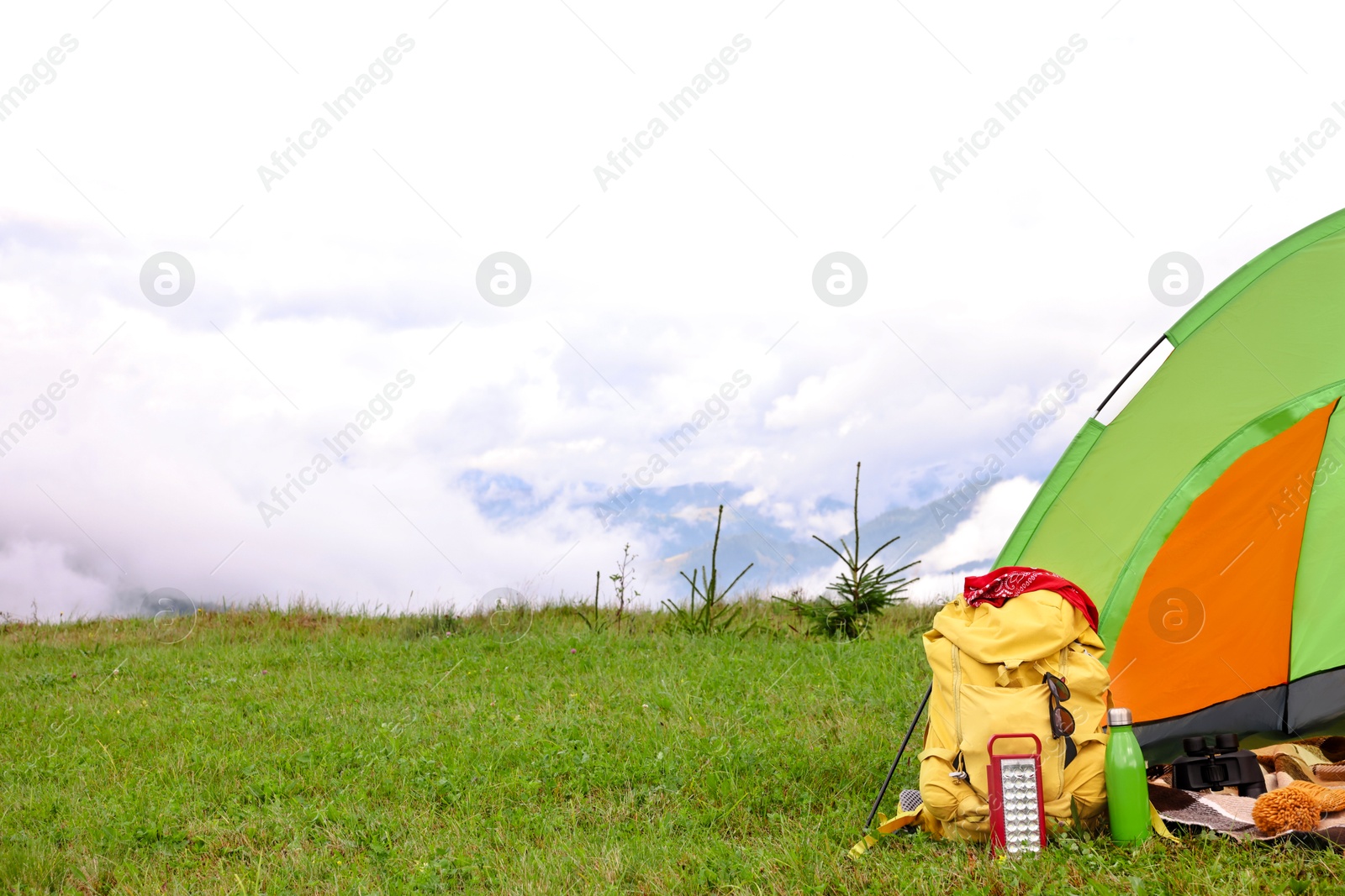 Photo of Tent, backpack and camping equipment on green grass in mountains, space for text