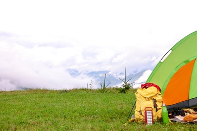 Photo of Tent, backpack and camping equipment on green grass in mountains, space for text