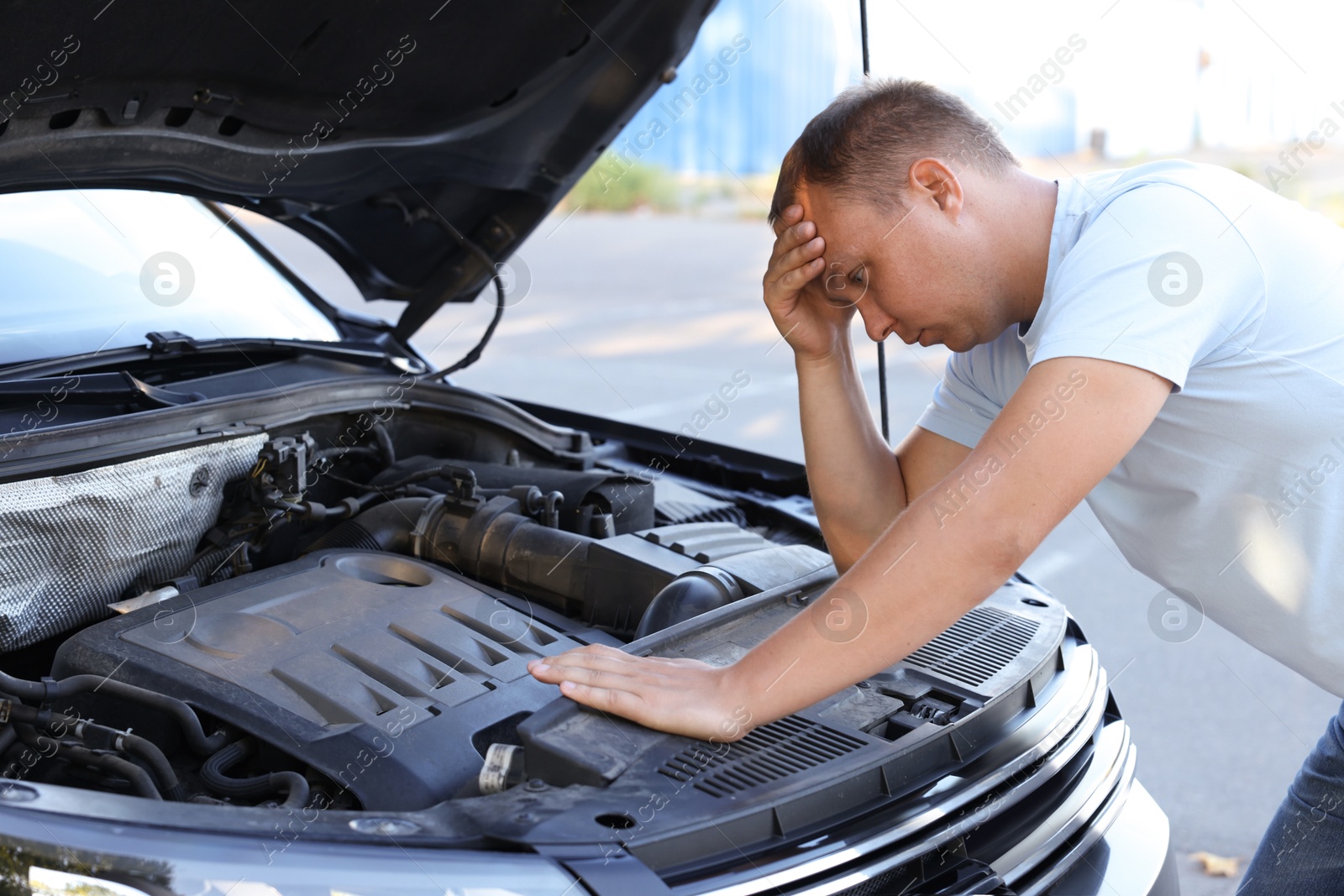 Photo of Stressed man looking under hood of broken car outdoors