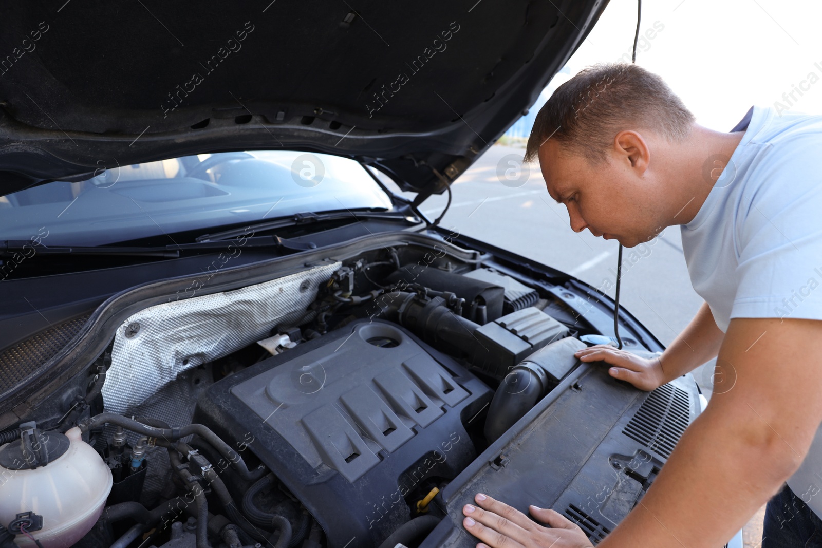 Photo of Stressed man looking under hood of broken car outdoors