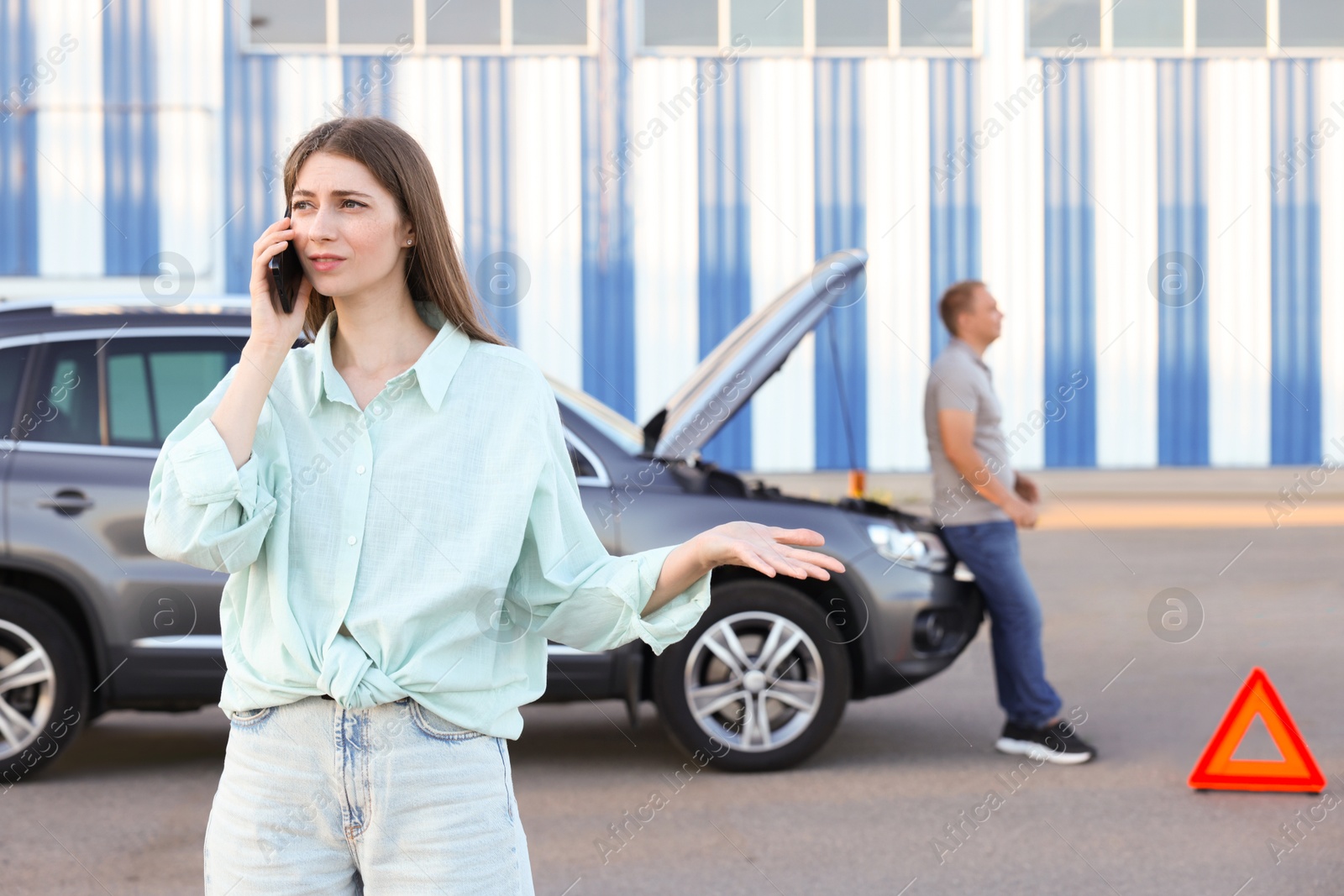 Photo of Man standing near broken auto while woman calling to car service outdoors