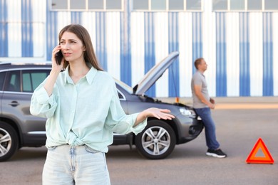 Man standing near broken auto while woman calling to car service outdoors