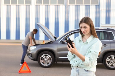 Man standing near broken car while woman using smartphone outdoors