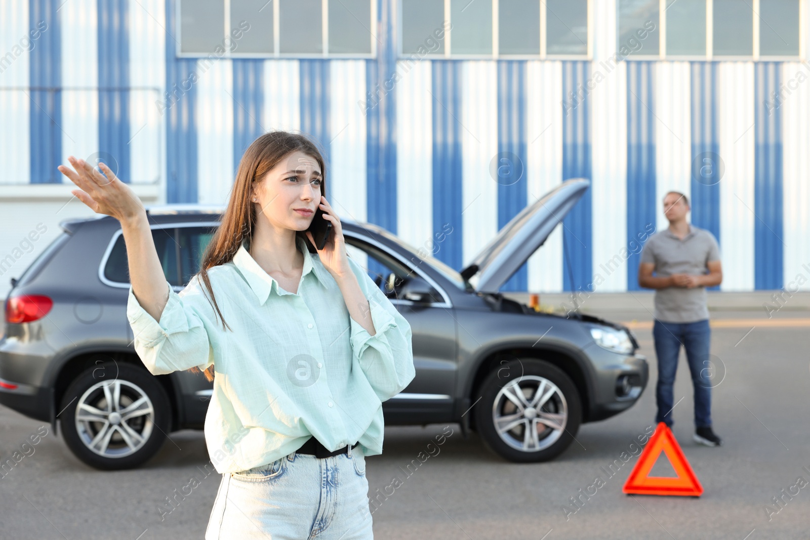 Photo of Man standing near broken auto while woman calling to car service outdoors