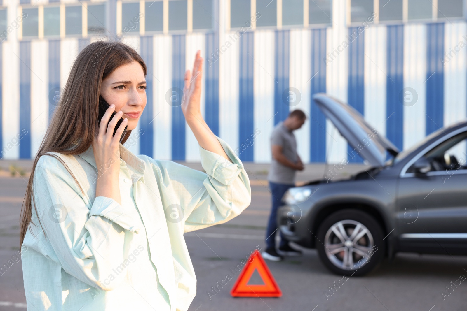 Photo of Man standing near broken auto while woman calling to car service outdoors