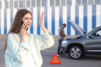 Photo of Man standing near broken auto while woman calling to car service outdoors