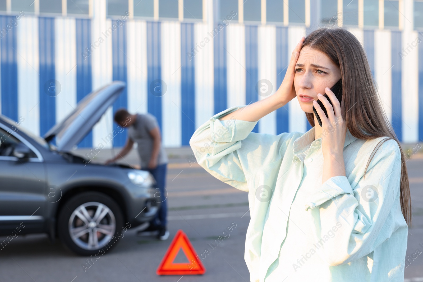 Photo of Man standing near broken auto while woman calling to car service outdoors