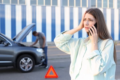 Man standing near broken auto while woman calling to car service outdoors