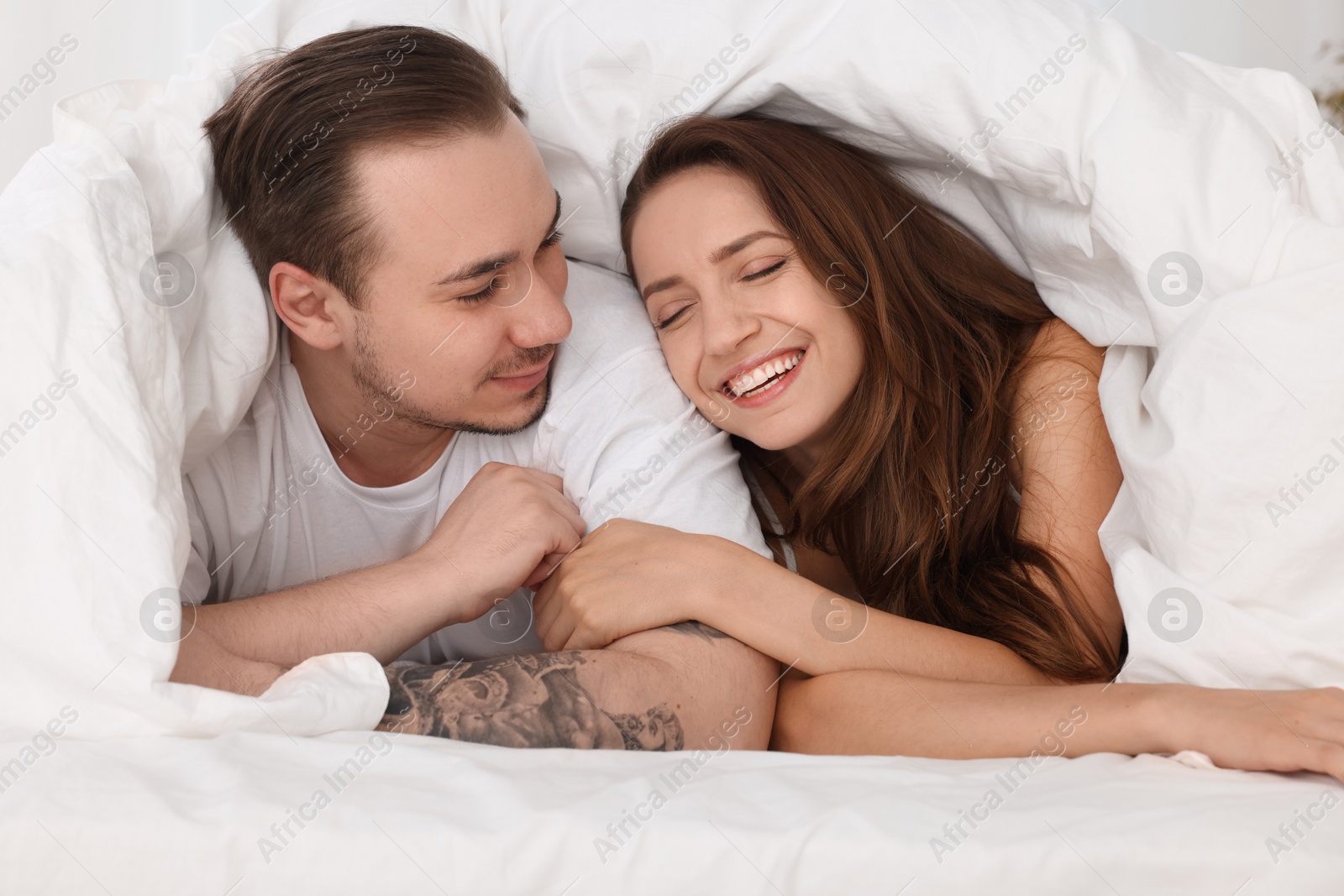 Photo of Happy couple spending time together wrapping in duvet in bed at home