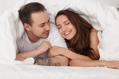 Happy couple spending time together wrapping in duvet in bed at home