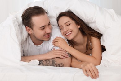 Happy couple spending time together wrapping in duvet in bed at home