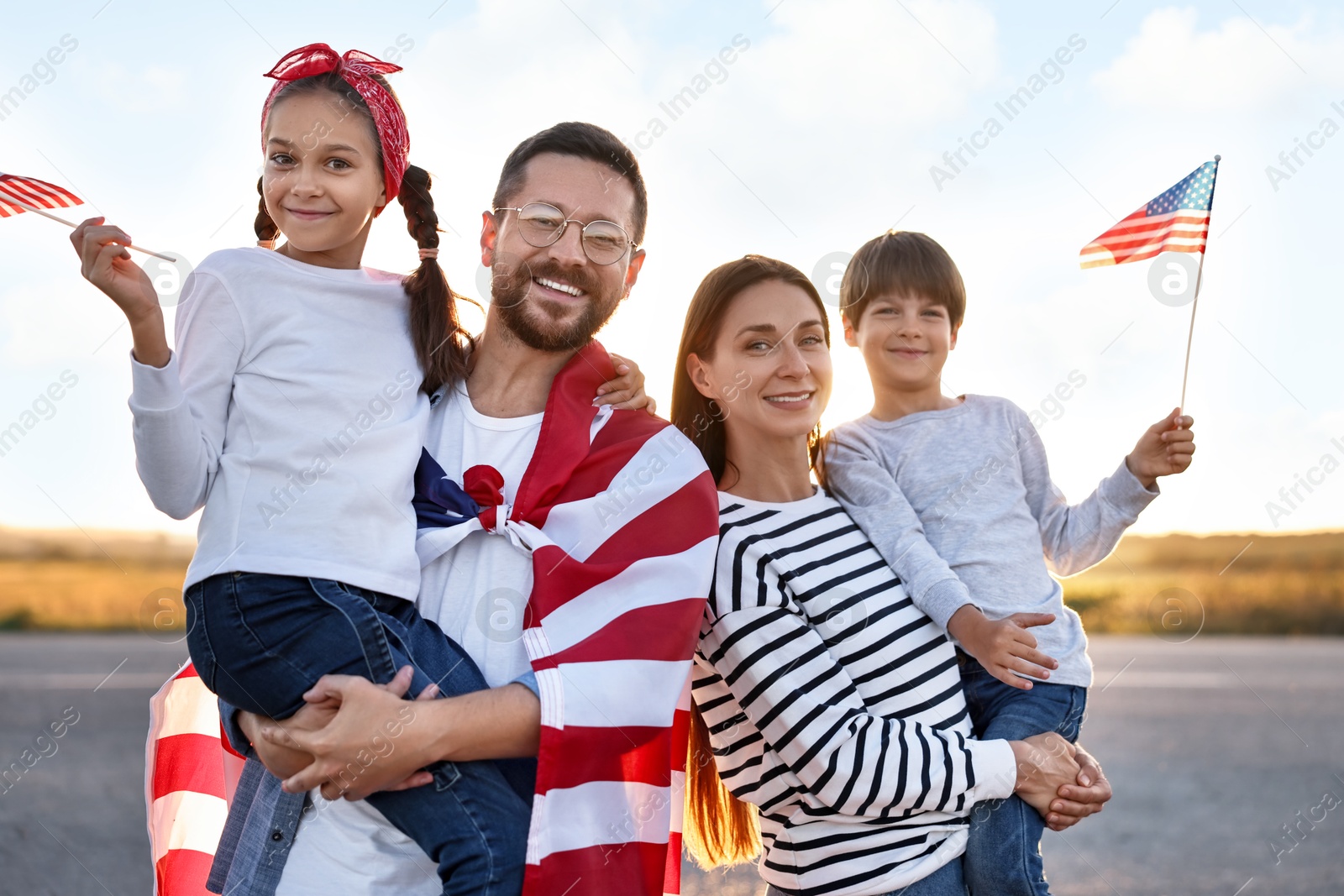 Photo of Family portrait of happy parents with children waving USA flags outdoors