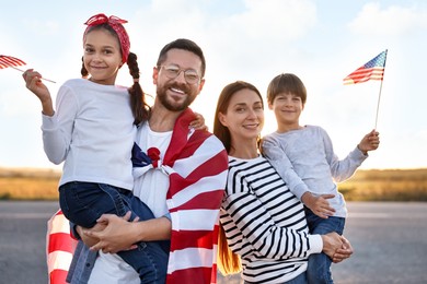 Family portrait of happy parents with children waving USA flags outdoors