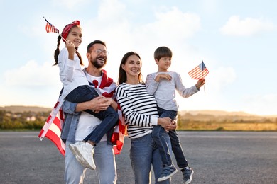 Photo of Family portrait of happy parents with children waving USA flags outdoors