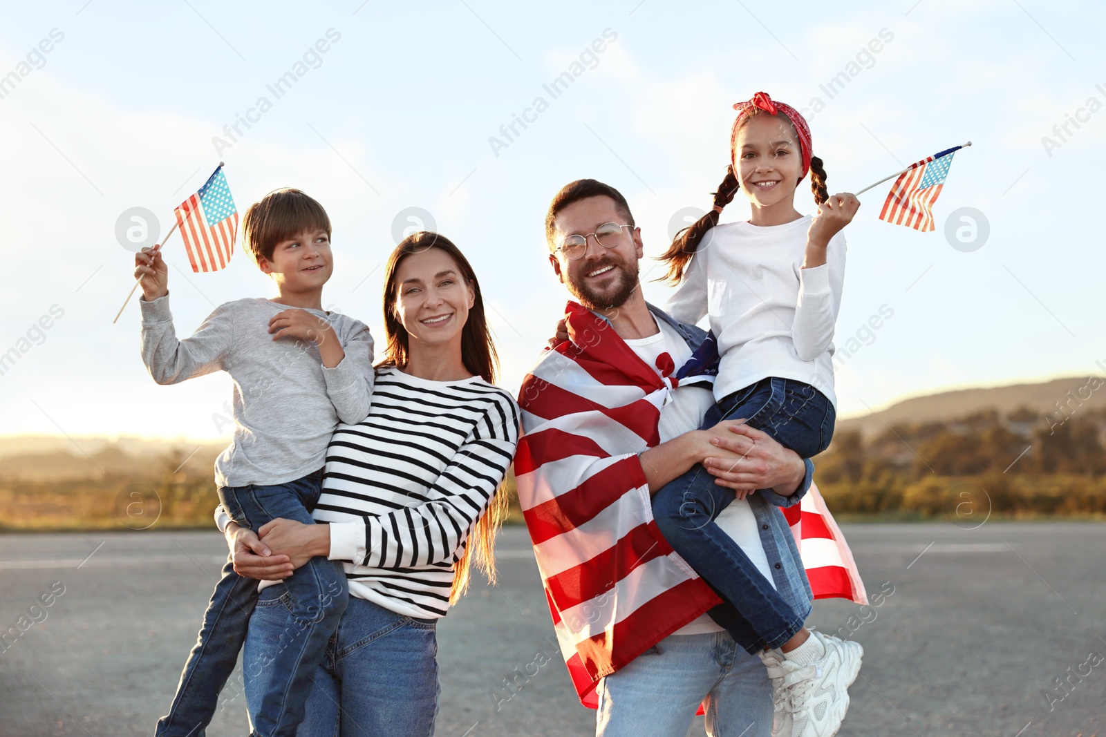 Photo of Family portrait of happy parents with children waving USA flags outdoors