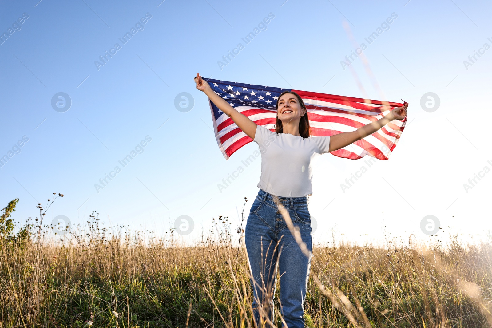 Photo of Happy woman with flag of USA outdoors, low angle view. Space for text