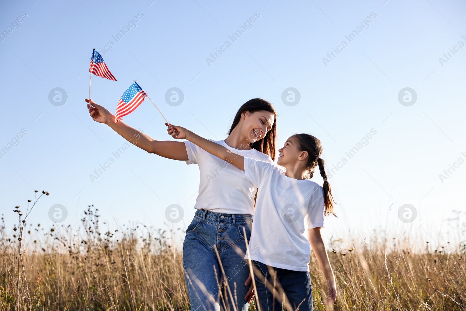 Photo of Happy mother and daughter with flags of USA outdoors, low angle view