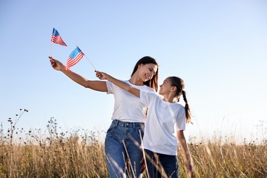 Happy mother and daughter with flags of USA outdoors, low angle view