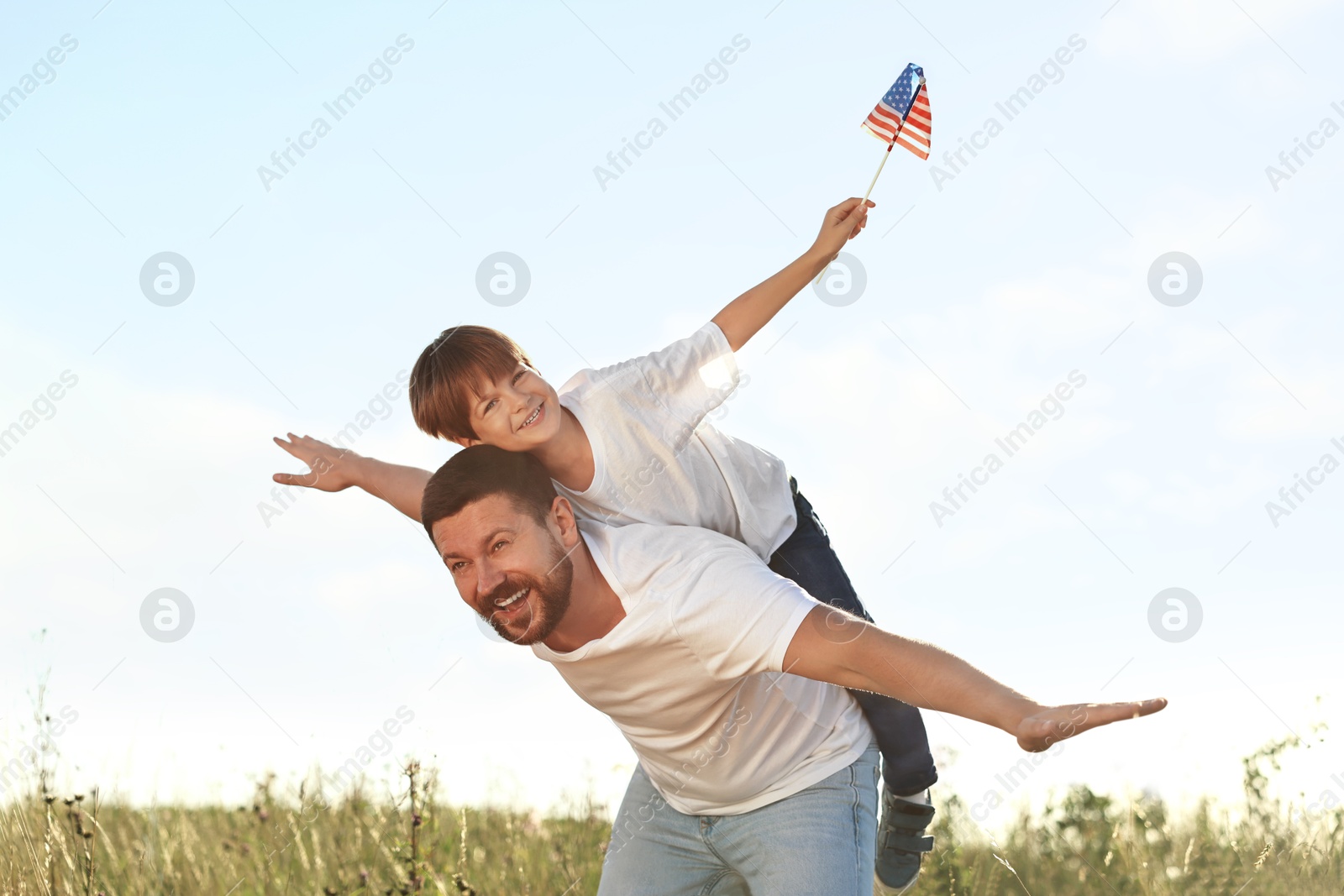 Photo of Happy father and son with flag of USA having fun outdoors