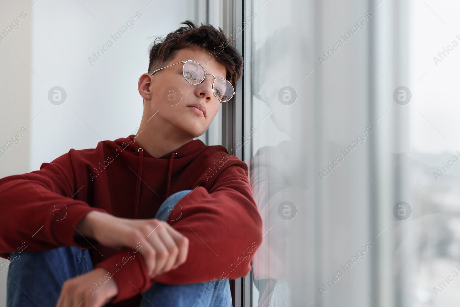 Photo of Loneliness concept. Sad teenage boy near window indoors, space for text