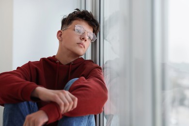 Loneliness concept. Sad teenage boy near window indoors, space for text