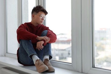 Loneliness concept. Sad teenage boy on windowsill indoors