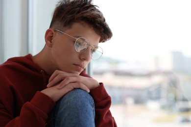 Photo of Loneliness concept. Sad teenage boy near window indoors, space for text