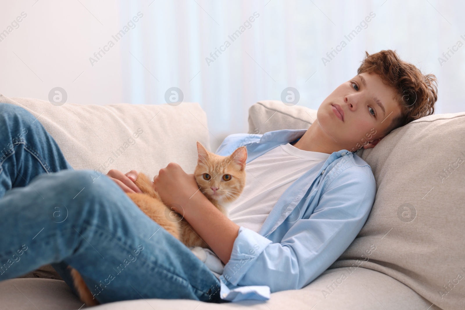 Photo of Loneliness concept. Sad teenage boy with cute cat on sofa at home