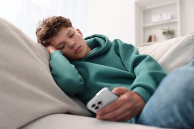 Loneliness concept. Sad teenage boy using smartphone on sofa at home