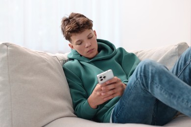 Loneliness concept. Sad teenage boy using smartphone on sofa at home