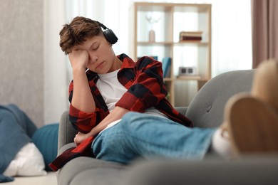 Loneliness concept. Sad teenage boy in headphones listening to music on sofa at home