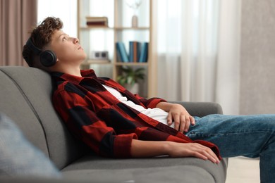 Loneliness concept. Sad teenage boy in headphones listening to music on sofa at home