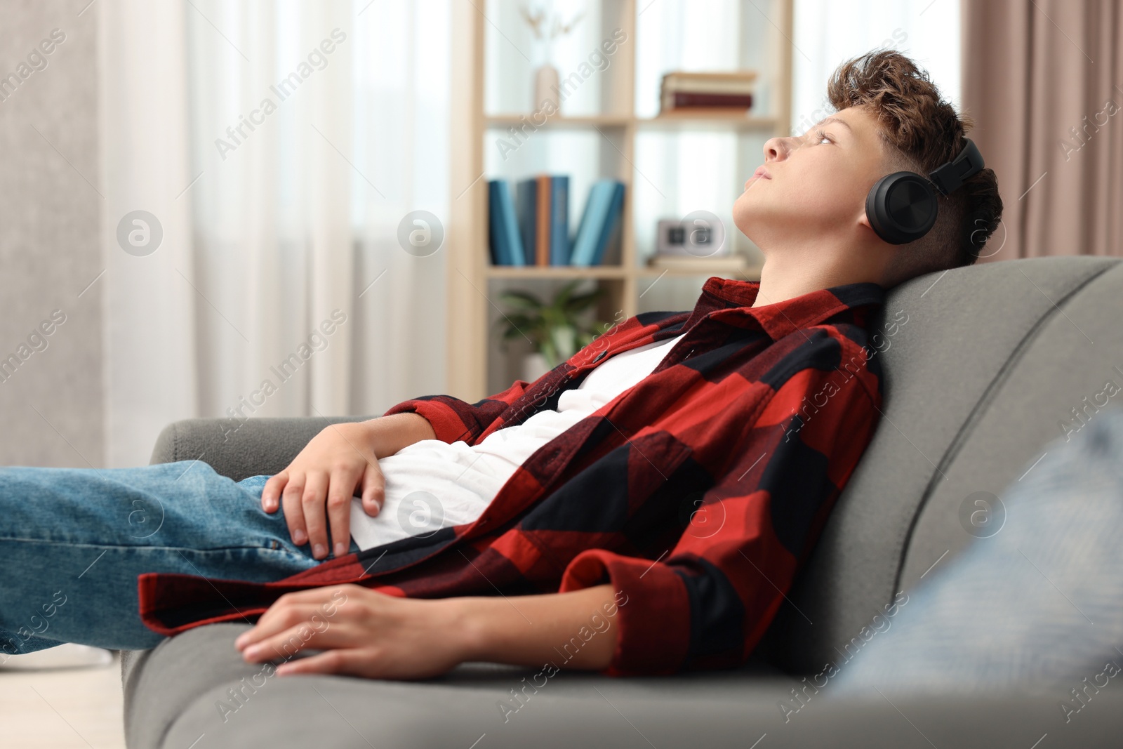 Photo of Loneliness concept. Sad teenage boy in headphones listening to music on sofa at home