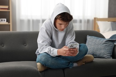 Photo of Loneliness concept. Sad teenage boy using smartphone on sofa at home