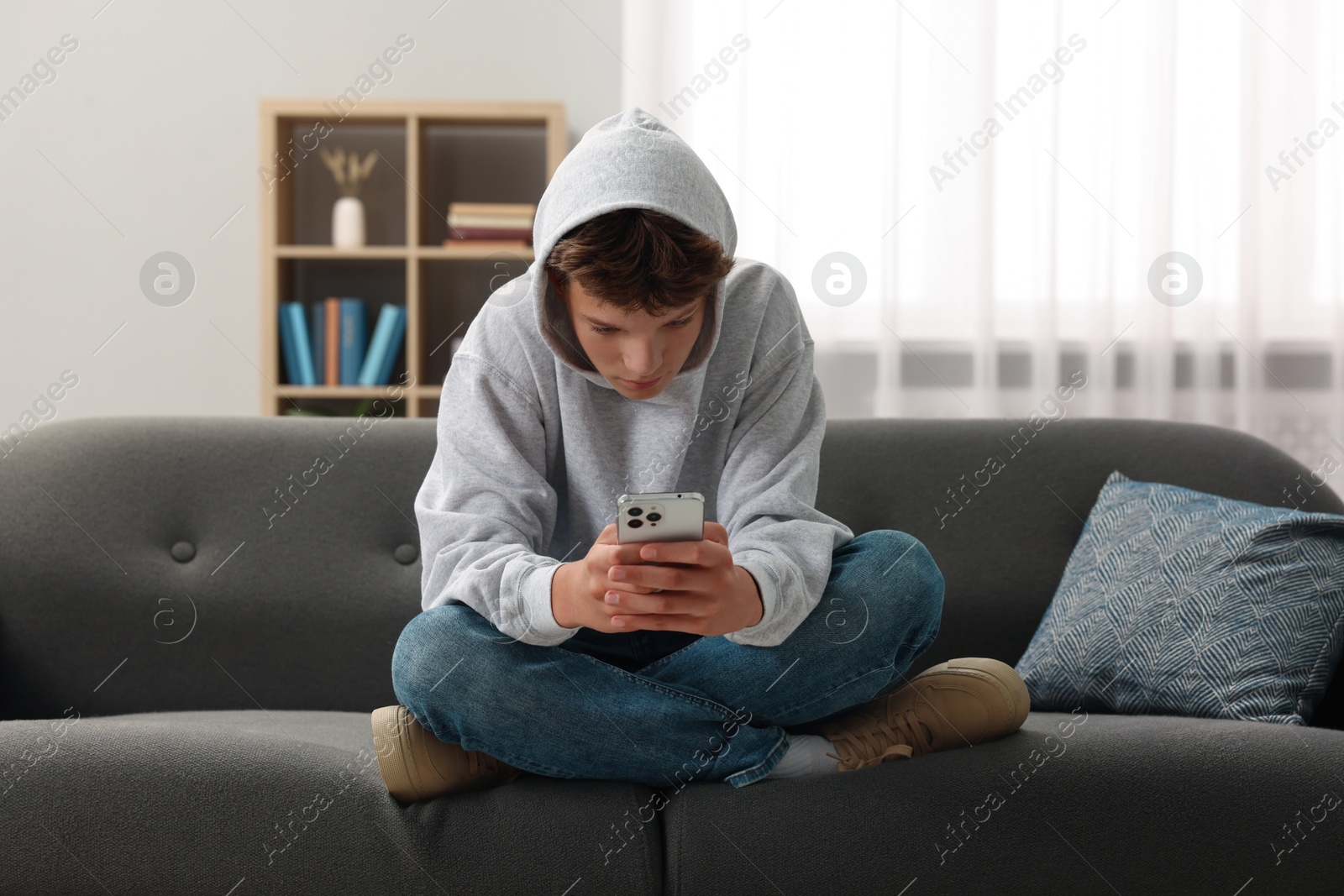 Photo of Loneliness concept. Sad teenage boy using smartphone on sofa at home