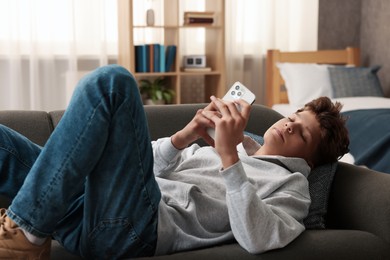 Loneliness concept. Sad teenage boy using smartphone on sofa at home