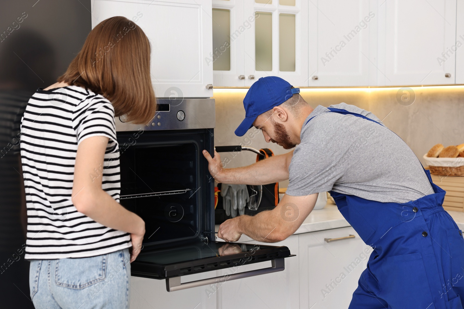 Photo of Woman looking how repairman fixing oven in kitchen