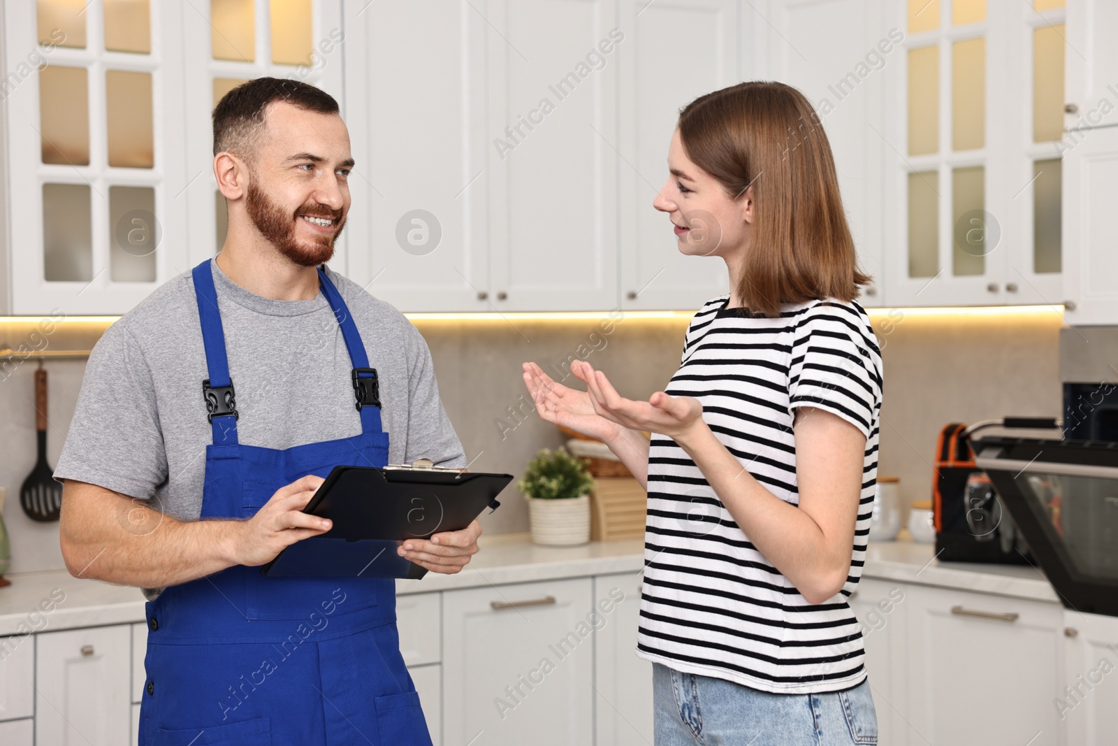 Photo of Woman talking with smiling repairman near oven in kitchen